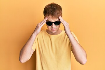 Young caucasian man wearing stylish sunglasses with hand on head, headache because stress. suffering migraine.