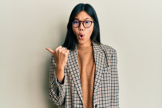 Young chinese woman wearing business style and glasses surprised pointing with hand finger to the side, open mouth amazed expression.