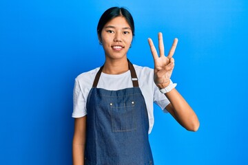 Young chinese woman wearing waiter apron showing and pointing up with fingers number three while...