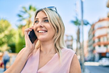 Young blonde woman smiling happy talking on the smartphone at the city.
