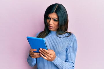 Young latin transsexual transgender woman using touchpad device in shock face, looking skeptical...