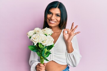 Young latin transsexual transgender woman holding flowers doing ok sign with fingers, smiling friendly gesturing excellent symbol