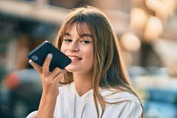 Caucasian sporty teenager girl sending voice message using smartphone at the city.