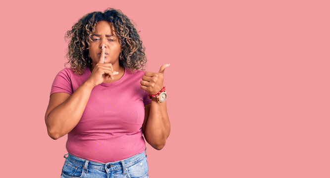 Young african american plus size woman wearing casual clothes asking to be quiet with finger on lips pointing with hand to the side. silence and secret concept.