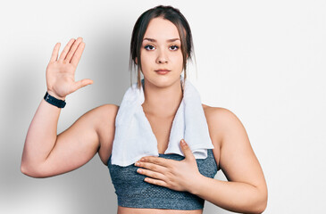 Young hispanic girl wearing sportswear and towel swearing with hand on chest and open palm, making...