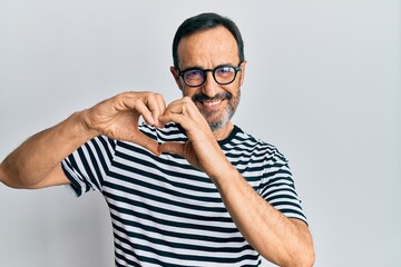 Middle age hispanic man wearing casual clothes and glasses smiling in love doing heart symbol shape with hands. romantic concept.