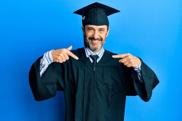 Middle age hispanic man wearing graduation cap and ceremony robe looking confident with smile on face, pointing oneself with fingers proud and happy.