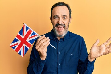 Middle age hispanic man holding united kingdom flag celebrating achievement with happy smile and winner expression with raised hand