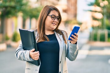 Young plus size businesswoman using smartphone holding binder at the city