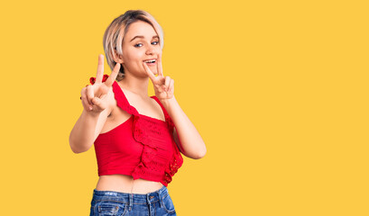 Young beautiful blonde woman wearing casual clothes smiling looking to the camera showing fingers...