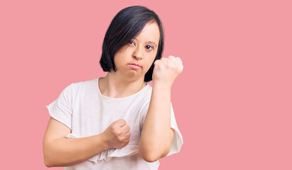 Fototapeta premium Brunette woman with down syndrome wearing casual white tshirt ready to fight with fist defense gesture, angry and upset face, afraid of problem