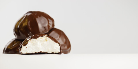 In a gray-and-white background, a group of chocolate-covered marshmallows is blurred. In the foreground in focus, half a marshmallow close-up with a place for text.