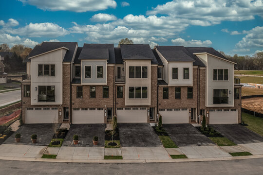 New American five unit townhouse complex with double car garage and balcony on a new real estate development in Maryland with cloudy blue sky