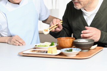 食事をする高齢者男性とエプロン姿の男性介護士
