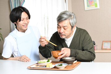 食事をする高齢者男性とエプロン姿の男性介護士