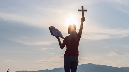 Silhouette of human praying and holding christian cross for worshipping God at sunset background....