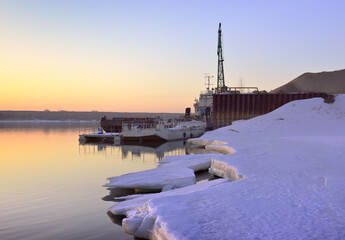 Morning on the bank of the Ob. The snowy edge of ice on the river in spring, the port pier against...