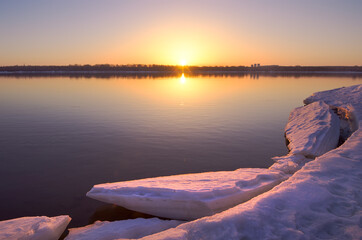 Morning on the bank of the Ob. A broken ice floe on the surface of the river water, the rising sun on the horizon. Novosibirsk, Siberia, Russia