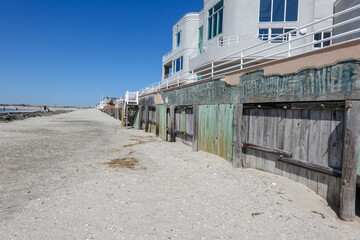 View along a beach with a worn wooden flood wall protecting the beachfront homes