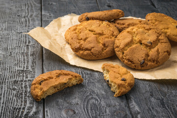 Freshly baked homemade cookies with chocolate chips on a piece of paper on a wooden table.