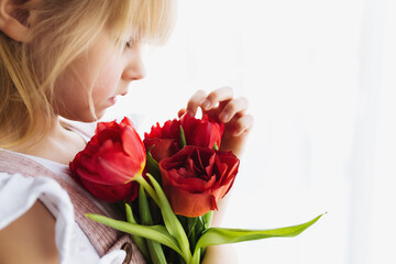 Obraz na płótnie Canvas Smiling small girl holding bouquet of red tulips. Concept for greeting card