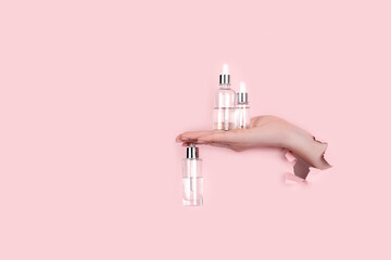 Female hand holding a transparent bottle of hyaluronic acid. Top horizontal view copyspace. Abstract pink background