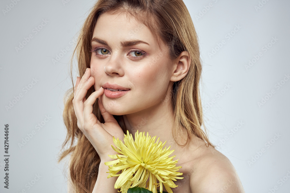 Wall mural portrait of a beautiful woman with a yellow flower on a light background cropped with copy space mod