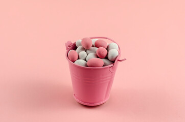Sweet multicolored dragee in a small bucket on a pink background