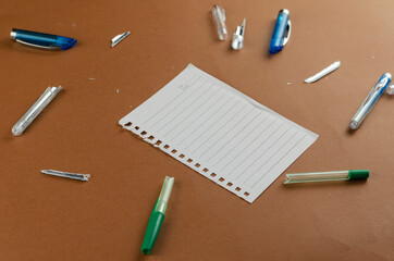 Broken pens and blank sheet of paper on brown table.
