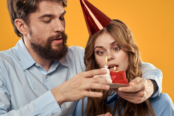 Birthday party man and woman in a cap with a cake on a yellow background cropped view