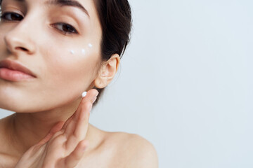 Pretty woman naked shoulders clean skin applies cream to face