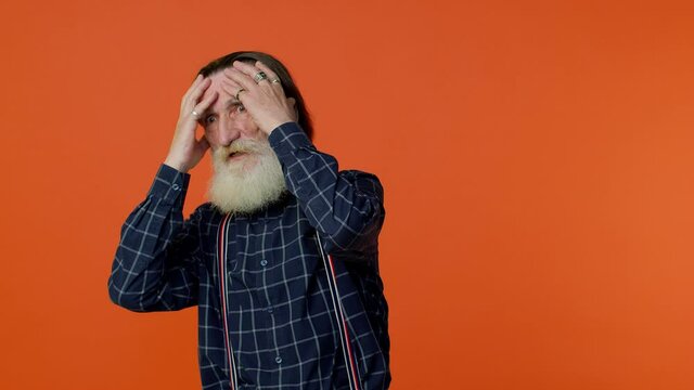 Stressed depressed mature old bearded gray-haired grandfather expresses his fear and waves his hands away from danger, waving no. Scared fearful senior man on orange background. People lifestyle