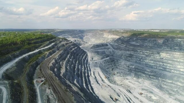 Aerial view panorama of Huge asbestos quarry with and railway. Inside the quarry there is a excavators and serpentine road for trucks. Summer sunny day. At the top of the quarry there is a forest
