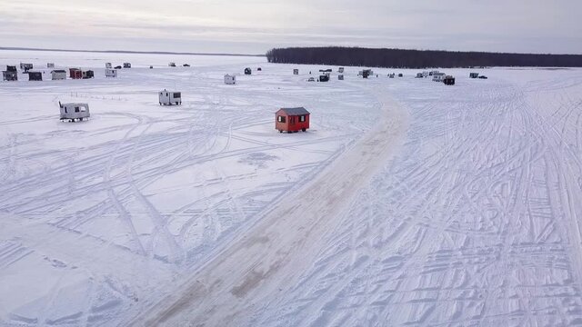Flying away from the village of ice fishing huts with a drone over the frozen lake with a partly cloudy sky