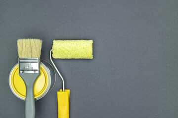 paintbrush with long bristles on can of yellow paint with paint roller on gray background. flat lay.