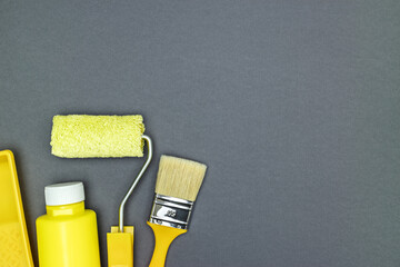 Fototapeta na wymiar tools for construction and decoration. paintbrush, roller and bottle of yellow paint on gray background, top view.