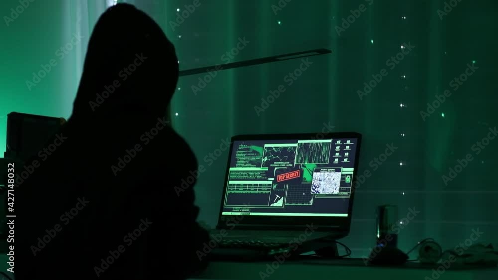 Poster a criminal hackergirl with black hood using laptop and big computers to hack network system from her