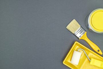 house renovation tools - paintbrush, roller with paint tray, can of yellow paint. gray background. top view.