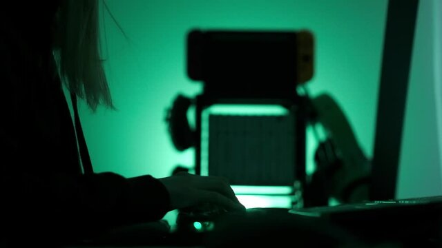 a criminal hackergirl with black hood using laptop and big computers to hack network system from her dark hacker neon room.