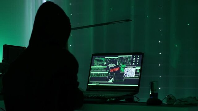 a criminal hackergirl with black hood using laptop and big computers to hack network system from her dark hacker neon room.
