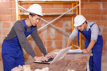 Portrait of two professional builders using laptop for reading plan of building