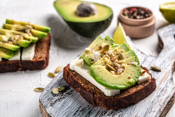 Healthy avocado toasts with rye bread, sliced avocado, cheese, pumpkin, nut and sesame for breakfast or lunch. Vegetarian food. Vegan menu. Food recipe background. Close up