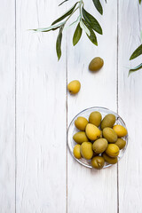 A bowl of green olives. Minimal still life of an olive branch and a glass bowl of olives on a white wooden table. Copy space