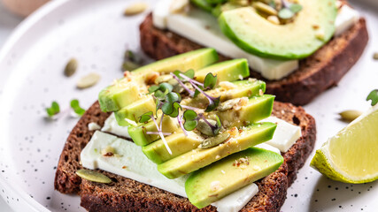 Healthy avocado toasts with rye bread, sliced avocado, cheese, pumpkin, nut and sesame for breakfast or lunch. Vegetarian food. Vegan menu. Food recipe background. Close up