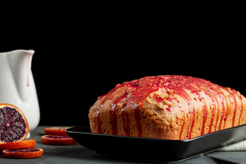 Closeup image of fresh homemade blood orange cake made in a loaf pan and served on black porcelain...