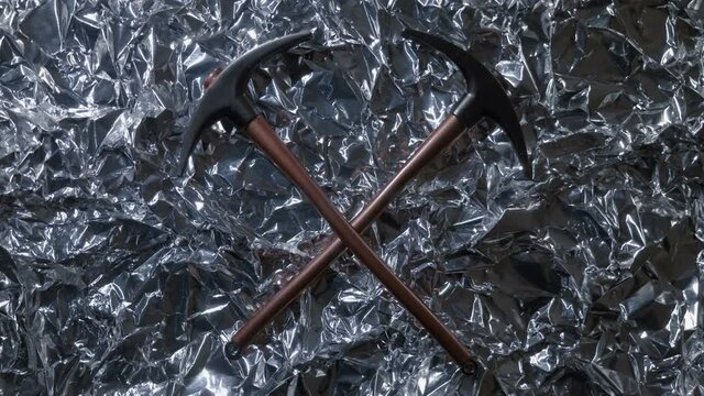 On a background from foil of silver color which shimmering of bright lights, two pickaxes as a symbol of the extractive industry , as well as the work of geologists looking for minerals are glitters 