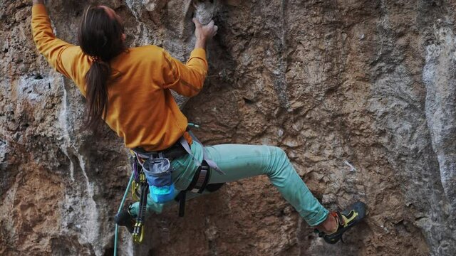 Rock climber in yellow sweatshirt on overhanging cliff. Male climber trying hard to grip handholds on tufas on challenging route and attaching quickdraw