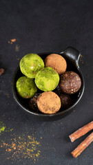 Super food. Energy balls in black bawl with cinnamon sticks. Homemade raw vegan fitness dessert covered by matcha tea powder and cocoa powder. Healthy eating. Ready to eat. Selective focus. Side view.
