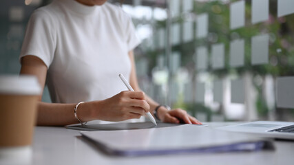 Fototapeta premium Cropped shot of businesswoman checking business data in digital tablet while sitting in modern office.