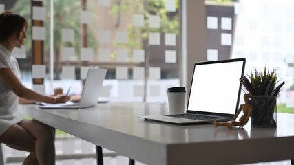 Mock up computer laptop with blank screen white table and businesswoman sitting in background.
